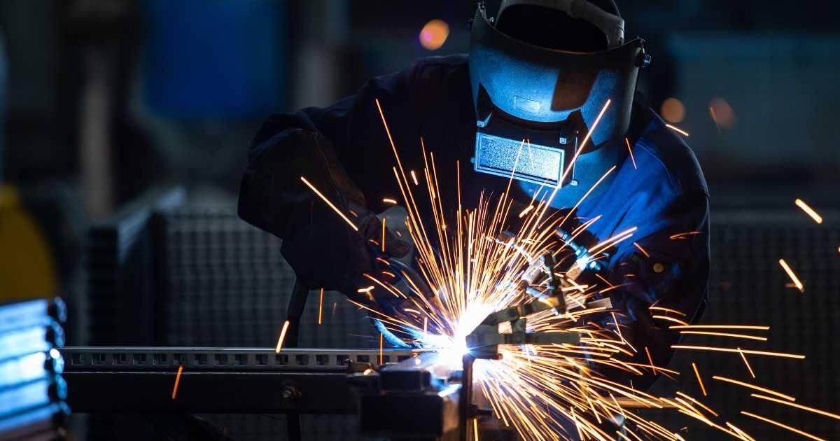 Welder in protective gear working with metal, surrounded by flying sparks.